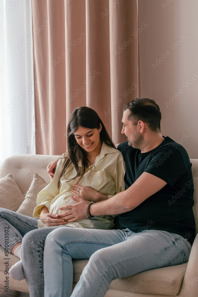 The husband hugs his pregnant wife, sitting at home on the couch..Family and pregnancy concept. The husband hugs his pregnant wife, sitting at home on the couch..Family and pregnancy concept.