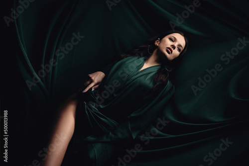fashionable photo of a beautiful woman with brunette hair in a dark green dress. Dress made of fabric fluttering creating a background