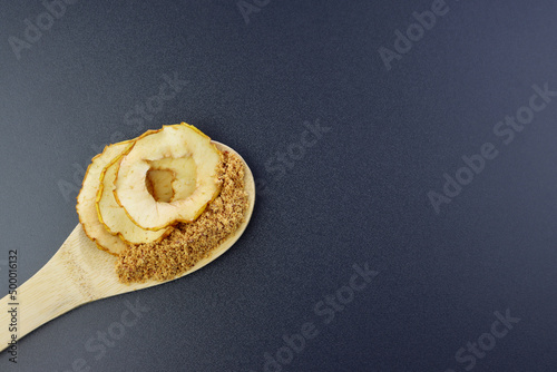 Dried apple slices and apple flour in a wooden spoon on a gray background. Apple fruit flour