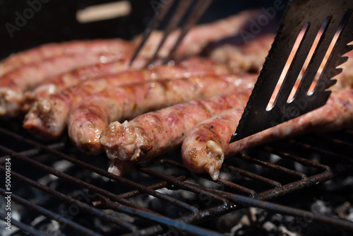 Sausages, traditional Italian 'salsiccia', being turned by a metal shovel, grill on a rustic grill over hot charcoal photo