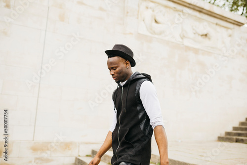 Young black male wearing a black hat walking down stairs on the street