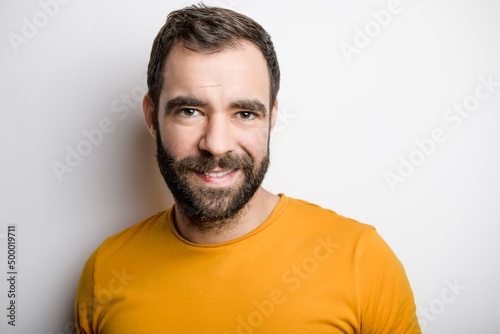 portrait of casual young man with beard and tattoo and Burnt Orange shirt on white background © Louis-Photo