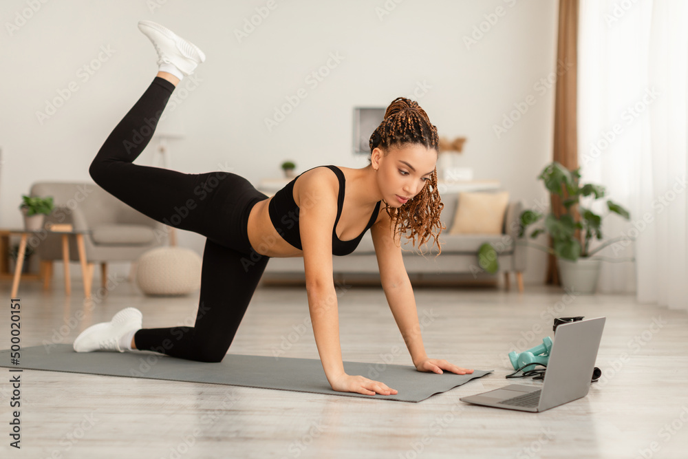 Fototapeta premium Sporty African Female Exercising Near Laptop On All Fours Indoors