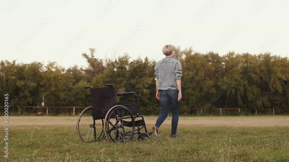 Disabled woman in wheelchair who has undergone physical therapy, surgery, medications and recovery, got up from wheelchair and walk ahead, back view Disabled woman in wheelchair who has undergone physical therapy, surgery, medications and recovery, got up from wheelchair and walk ahead, back view
