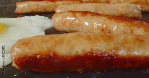 Macro probe footage of breakfast sausage and eggs being cooked on a griddle. 4K slider shot.