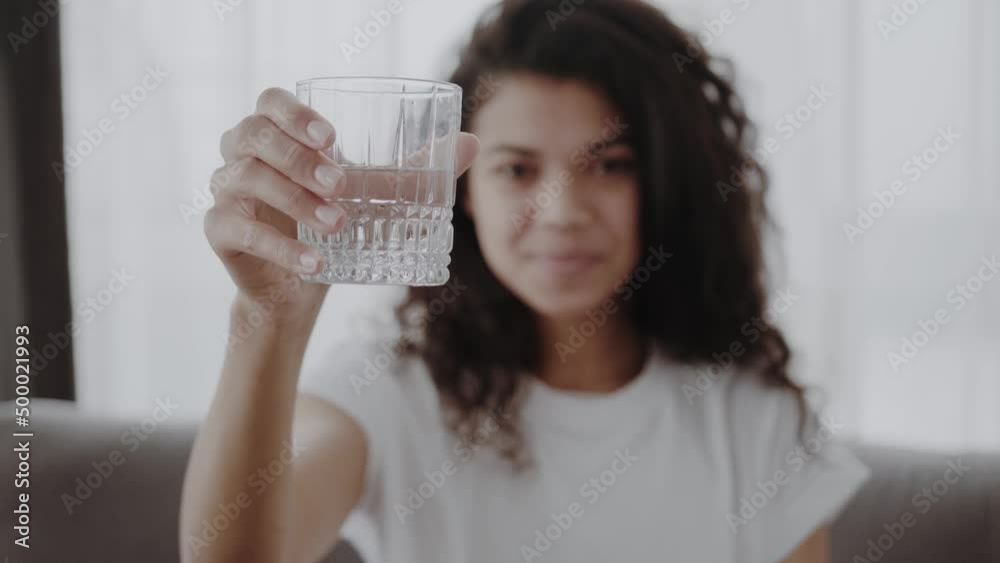Smiling African American woman offering glass of fresh pure mineral water at camera, beautiful young female recommending daily healthy lifestyle habit, healthcare and hydration Smiling African American woman offering glass of fresh pure mineral water at camera, beautiful young female recommending daily healthy lifestyle habit, healthcare and hydration