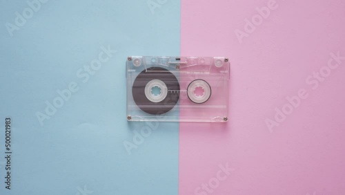 Stop motion of a playing audio cassette with a winding magnetic tape on a pink blue background. Retro 80s music concept. top view. flat lay
