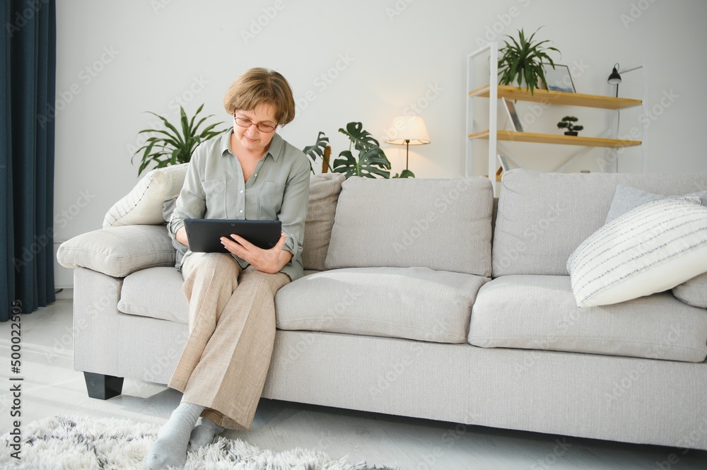 Senior woman looking and laughing at her digital tablet on sofa Senior woman looking and laughing at her digital tablet on sofa