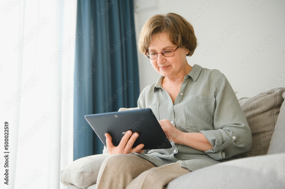 Retirement Leisure. Smiling Elderly Woman Resting With Digital Tablet On Couch At Home, Browsing Internet Or Watching Movies Retirement Leisure. Smiling Elderly Woman Resting With Digital Tablet On Couch At Home, Browsing Internet Or Watching Movies