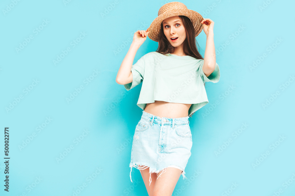 Portrait of young beautiful smiling female in trendy summer jeans skirt. carefree woman posing near blue wall in studio. Positive model having fun indoors. Cheerful and happy. In hat Portrait of young beautiful smiling female in trendy summer jeans skirt. carefree woman posing near blue wall in studio. Positive model having fun indoors. Cheerful and happy. In hat
