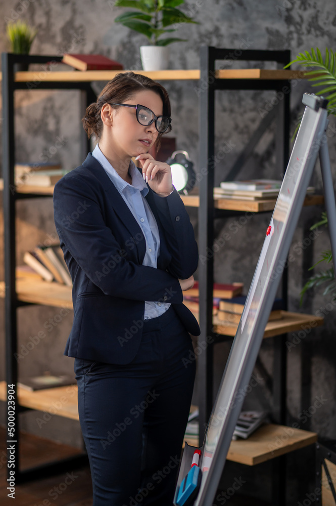 Naklejka premium Elegant dark-haired woman standing near flipchart