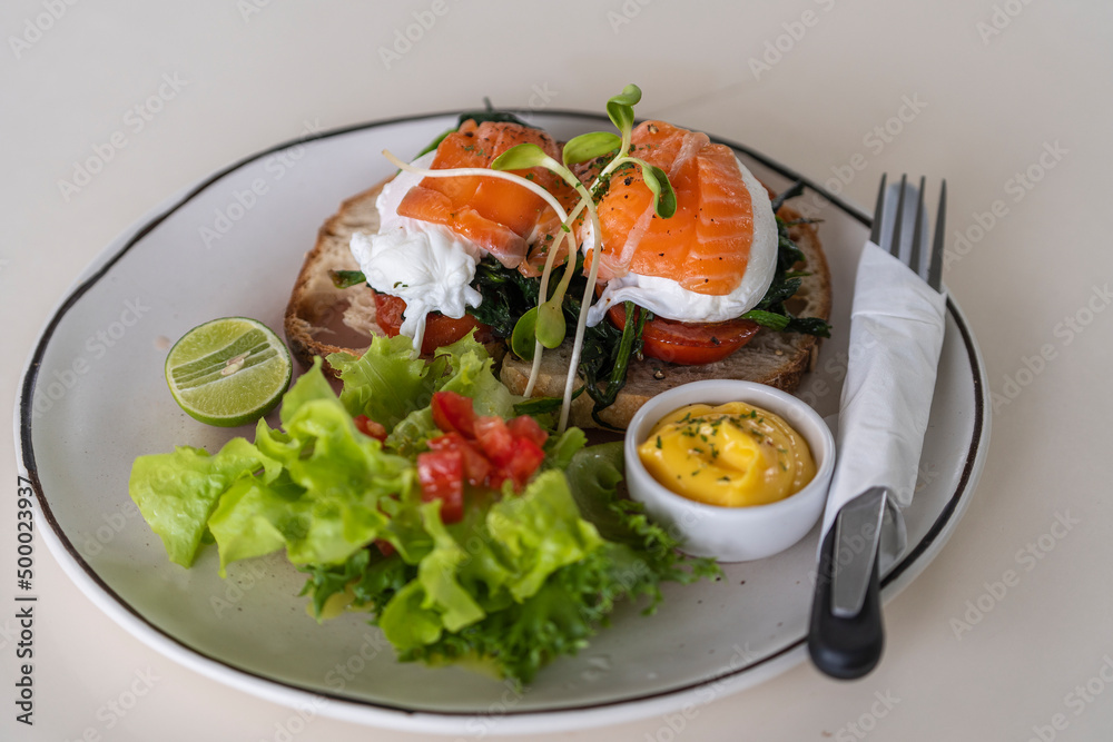 Toast with poached eggs, tomato and salmon on plate in cafe, breakfast time Toast with poached eggs, tomato and salmon on plate in cafe, breakfast time