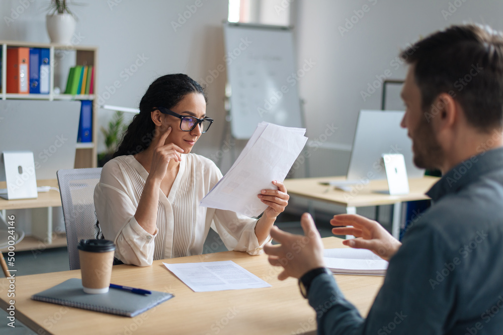 Personnel manager communicating with vacancy candidate, reading resume during job interview at office