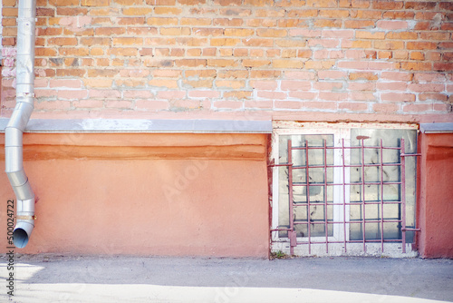 Brick wall, concrete brick, drainpipe, square basement window behind iron bars
