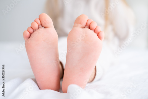 Close up kid child barefooted legs feet lying on white bed linen. Neutral pastel light color tones © Юля Шевцова