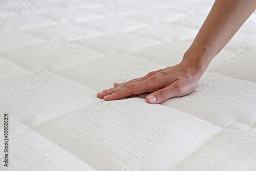 Cropped shot of young woman's hand testing white orthopedic matress on firmness. Female pressing hypoallergenic foam mattress surface to check its softness. Close up, copy space, top view, background. photo