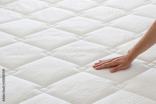 Cropped shot of young woman\'s hand testing white orthopedic matress on firmness. Female pressing hypoallergenic foam mattress surface to check its softness. Close up, copy space, top view, background.
