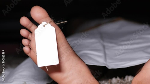 The dead man's body with blank tag on feet under white cloth in a morgue photo