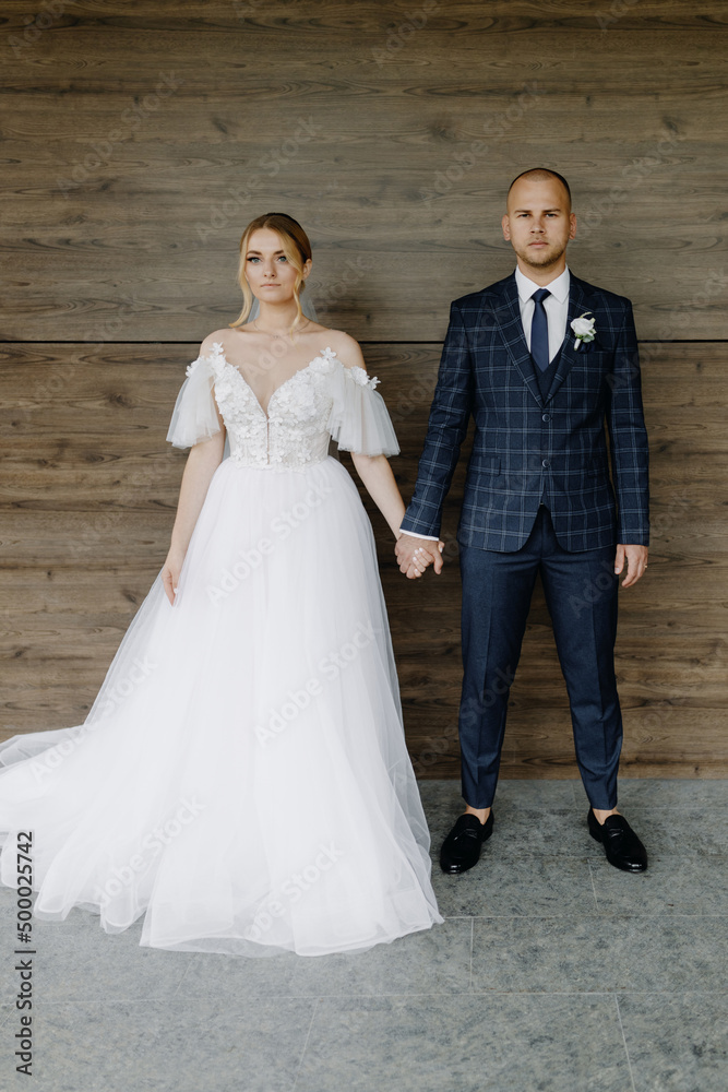 Beautiful couple of newlyweds holding hands on the background of the wall