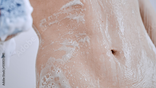 Closeup shot of a woman's wet soapy stomach while showering