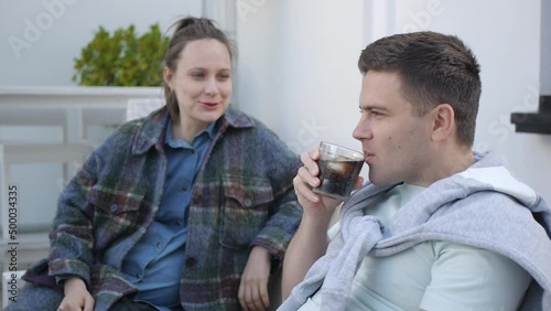 Young man laughing sipping carbonated soft drink from the glass with ice and lemon slice. Couple at the cafe terrace.