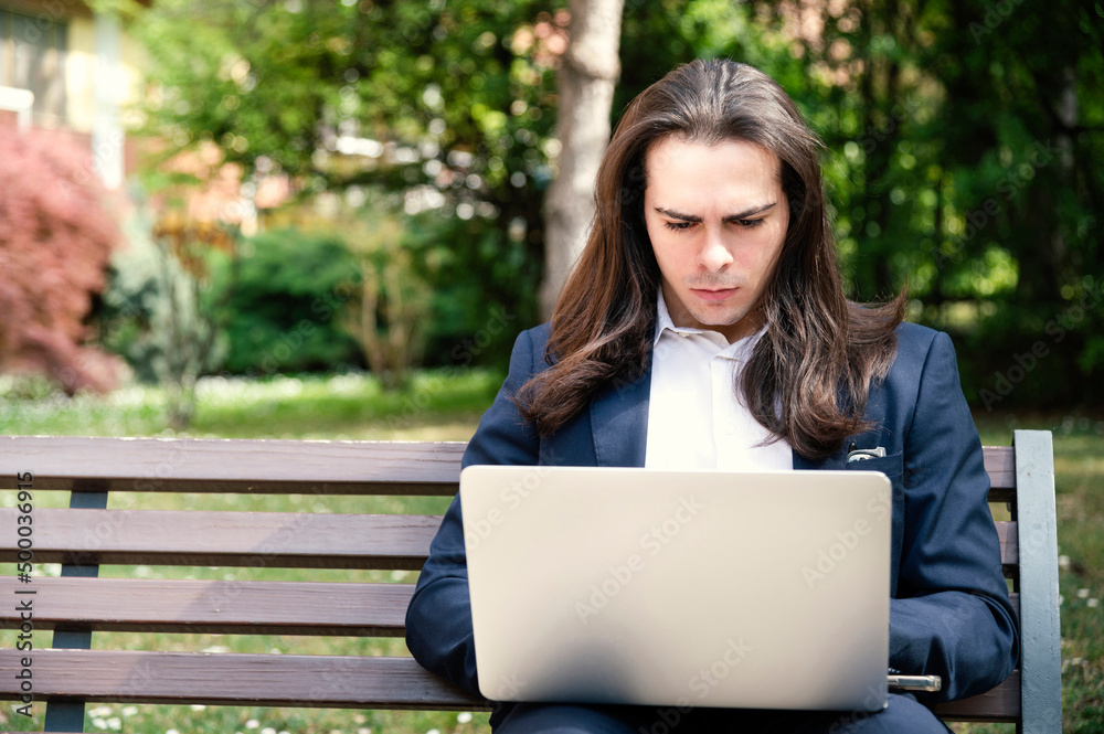 young man sitting on the bench consulting a laptop computer young man sitting on the bench consulting a laptop computer