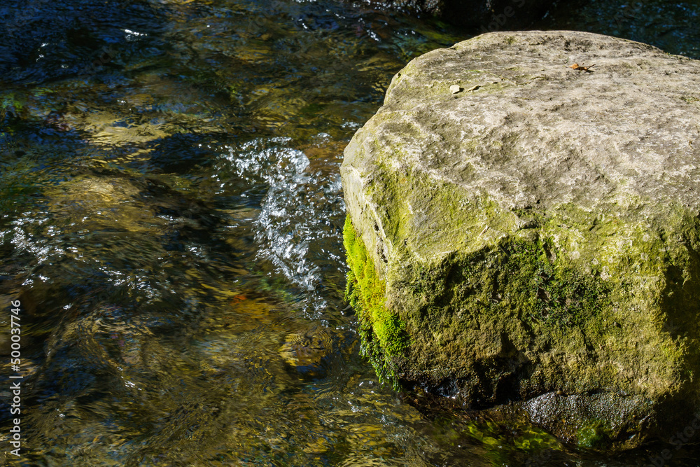 Stone in the water. Stone in the middle of the stream is covered with green moss. Stone in the water. Stone in the middle of the stream is covered with green moss.