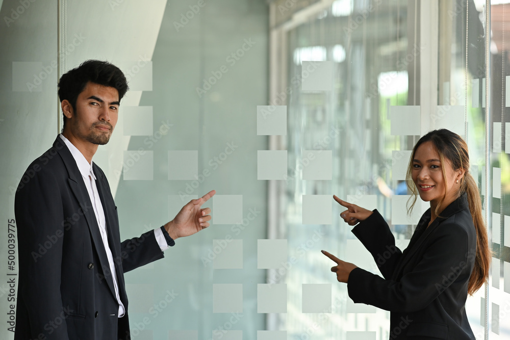 A portrait of Asian businesspeople standing in a workplace pointing fingers to the side, for business and technology concept. A portrait of Asian businesspeople standing in a workplace pointing fingers to the side, for business and technology concept.