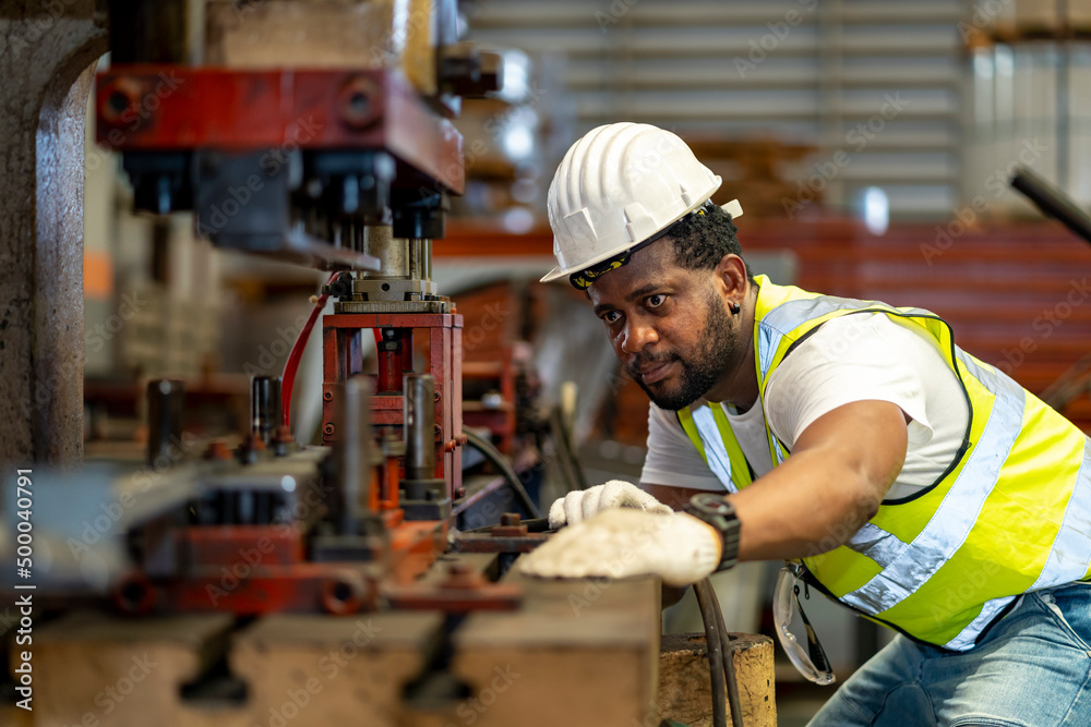 African American industrial worker is using hydraulic power press machine to make metal and steel part while working inside the metal sheet galvanized roof factory for safety industry concept African American industrial worker is using hydraulic power press machine to make metal and steel part while working inside the metal sheet galvanized roof factory for safety industry concept