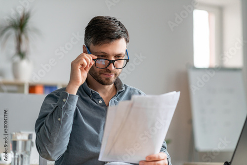 Busy mature male entrepreneur working with papers at workplace in office, checking financial reports photo