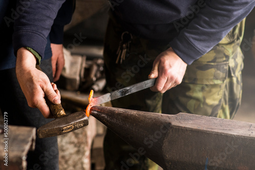 Blacksmith forges hinge on a anvil. Hammering hot red steel