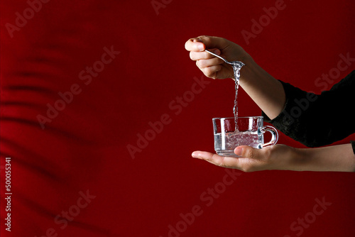 Girl holding a cup with cold liquid and stiring with a spoon near red wall with copy space photo