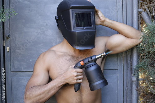 Shirtless welder holding a blowtorch photo