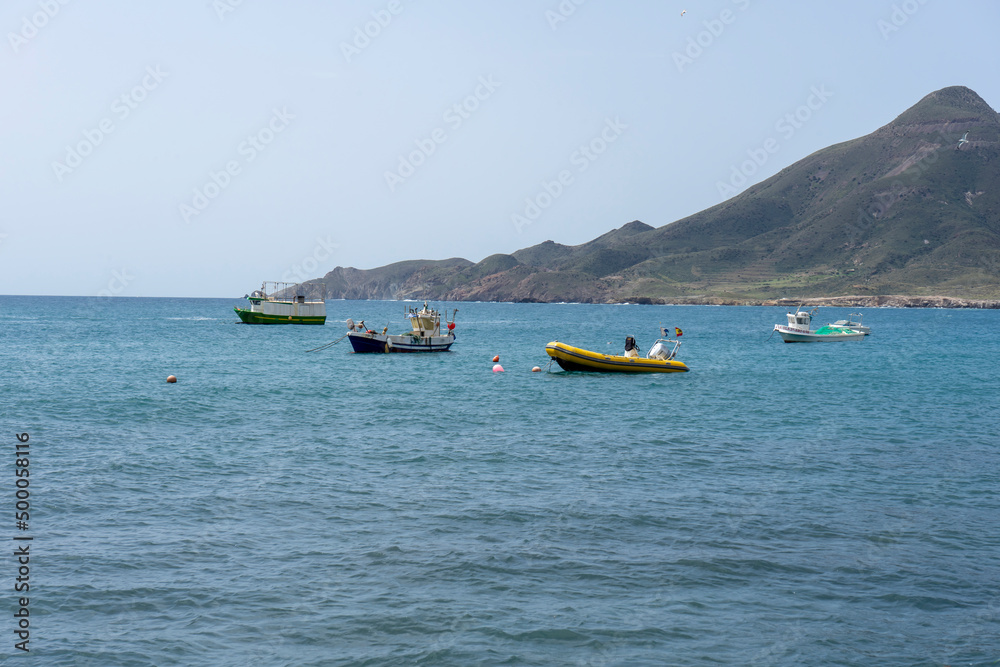 Fototapeta premium COLOURED BOATS IN THE SEA WITH A MOUNTAIN IN THE BACKGROUND