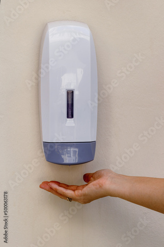 Photography Vertical shot of a woman's palm underneath a wall mounted hand sanitizer dispens
