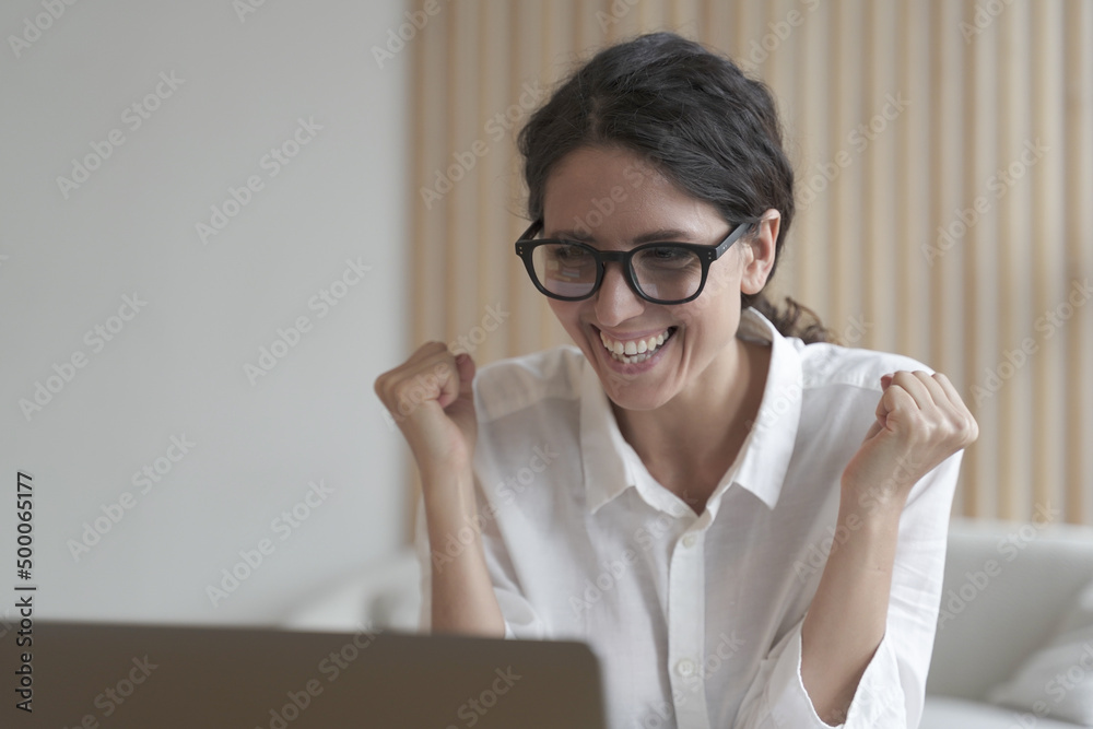 Overjoyed italian business woman clenching fists while getting pleasant news on computer Overjoyed italian business woman clenching fists while getting pleasant news on computer