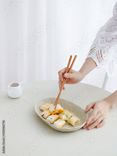 Adult female hands taking piece of Dan Bing (Taiwanese egg crepe) with wooden chopsticks