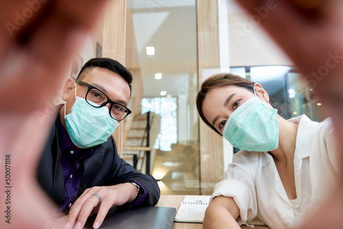 Businessman and woman take a selfie by mobile phone and wear the facial mask in office
