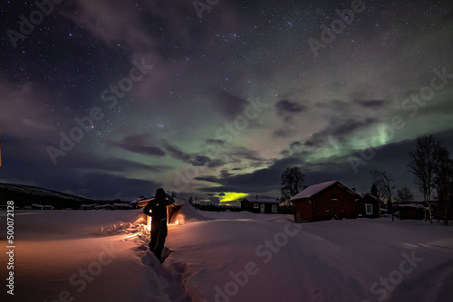 Northern Lights in the arctic winter with snow and chalets