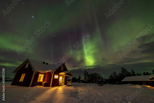 Northern Lights in the arctic winter with snow and chalets