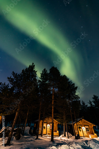 Northern Lights in the arctic winter with snow and chalets