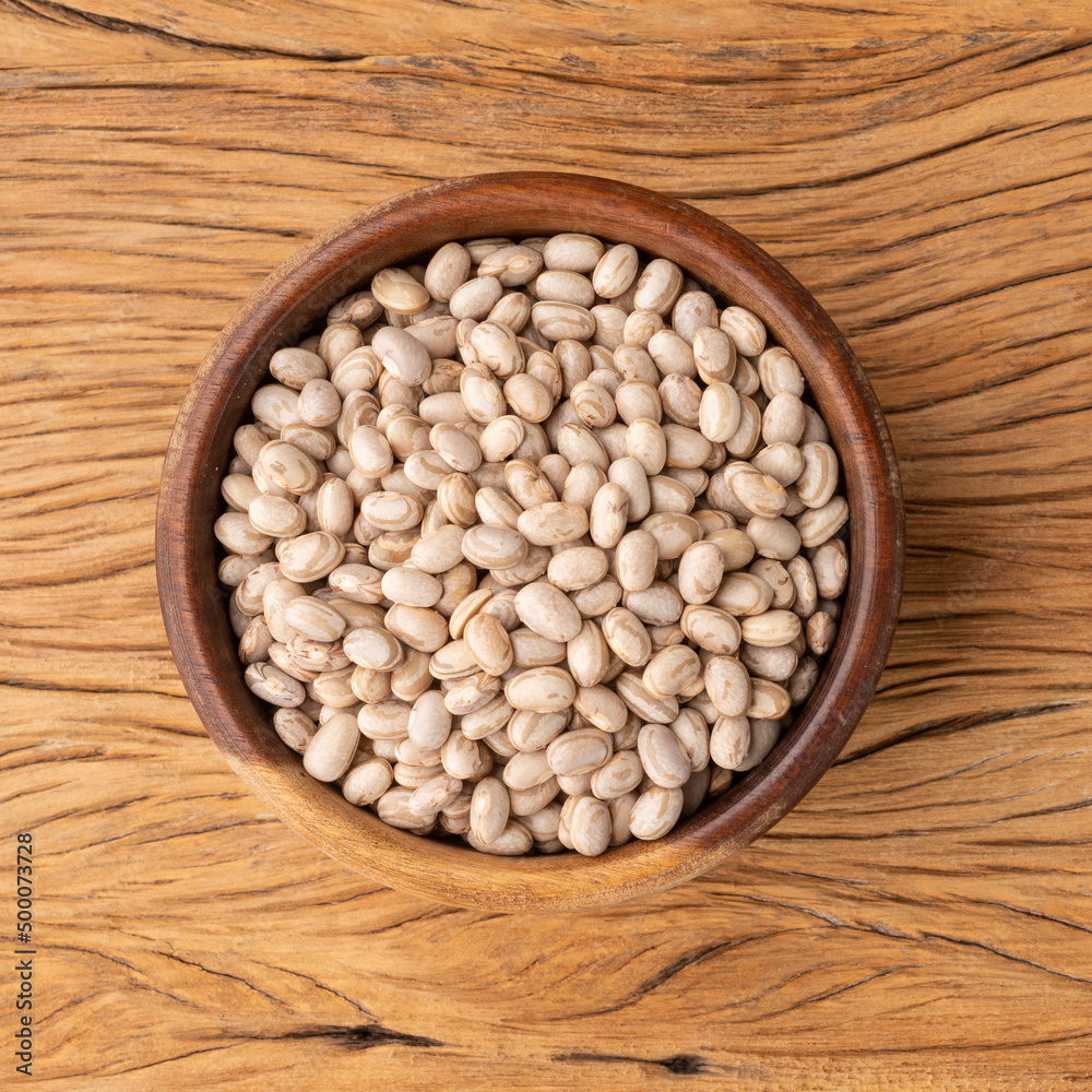 Raw brown beans in a wooden bowl over wooden table Raw brown beans in a wooden bowl over wooden table