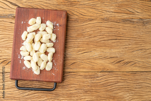 Uncooked italian pasta gnocchi on a board over wooden table with copy space