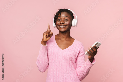 Black young woman pointing finger upward while listening music