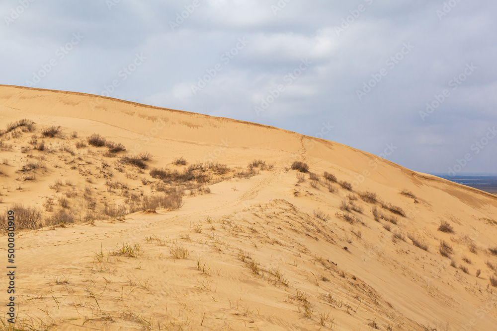 Sarykum dune. Dagestan, Russia. A unique sandy mountain in the Caucasus on a cloudy day. Grass grows on a sand dune.