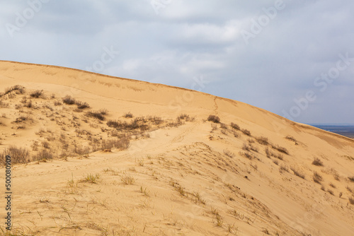 Sarykum dune. Dagestan, Russia. A unique sandy mountain in the Caucasus on a cloudy day. Grass grows on a sand dune.
