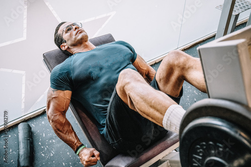 Obraz na plátně Muscle man trains legs on gym machine. Fitness