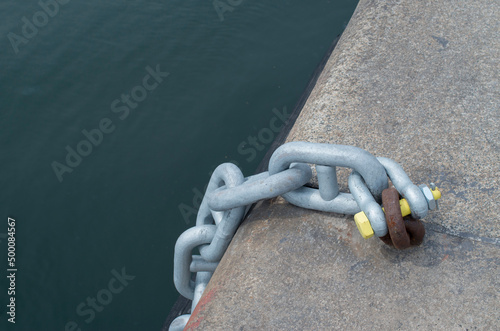 New metal chain attached with a shackle toold rusty ring in the port close photo