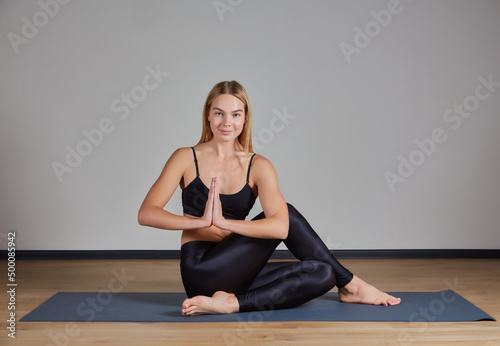 Calm young woman wearing black sportswear practicing yoga, doing Padmasana exercise, sitting in Lotus pose on mat, namaste hands