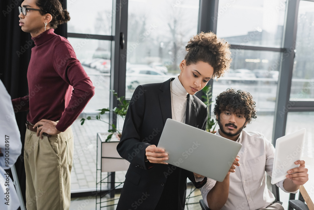 Multiethnic business people using devices near colleagues in office. Multiethnic business people using devices near colleagues in office.